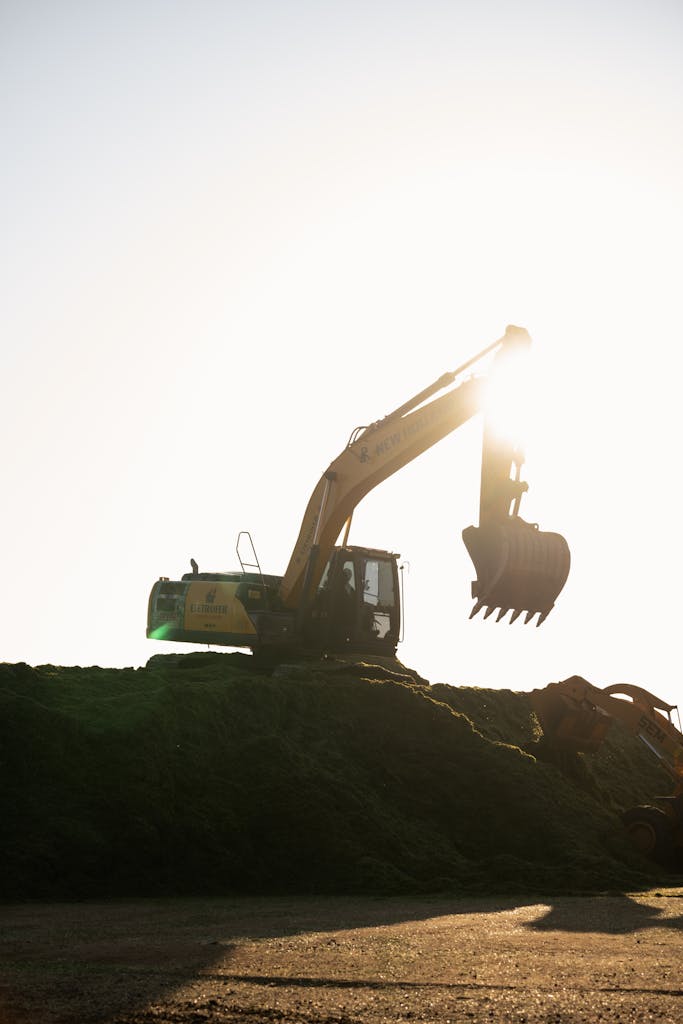 A silhouetted excavator works on a hill during a stunning sunset at a construction site.