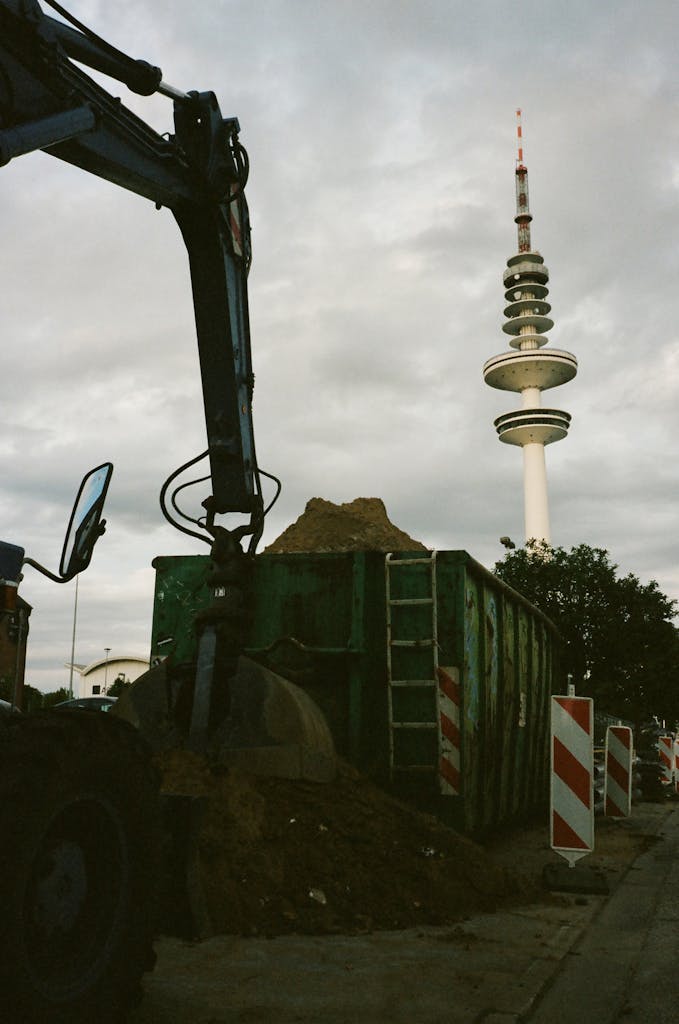 Construction site with excavator beside a distinctive urban telecommunications tower.