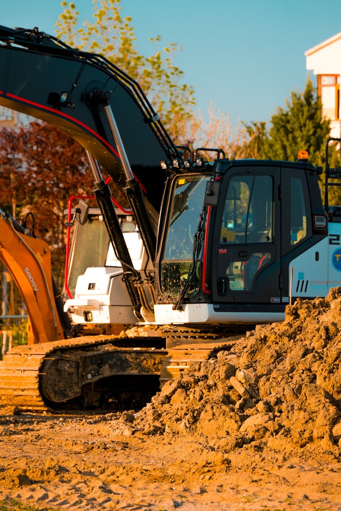 Excavator at a construction site with dirt piles and trees in background.